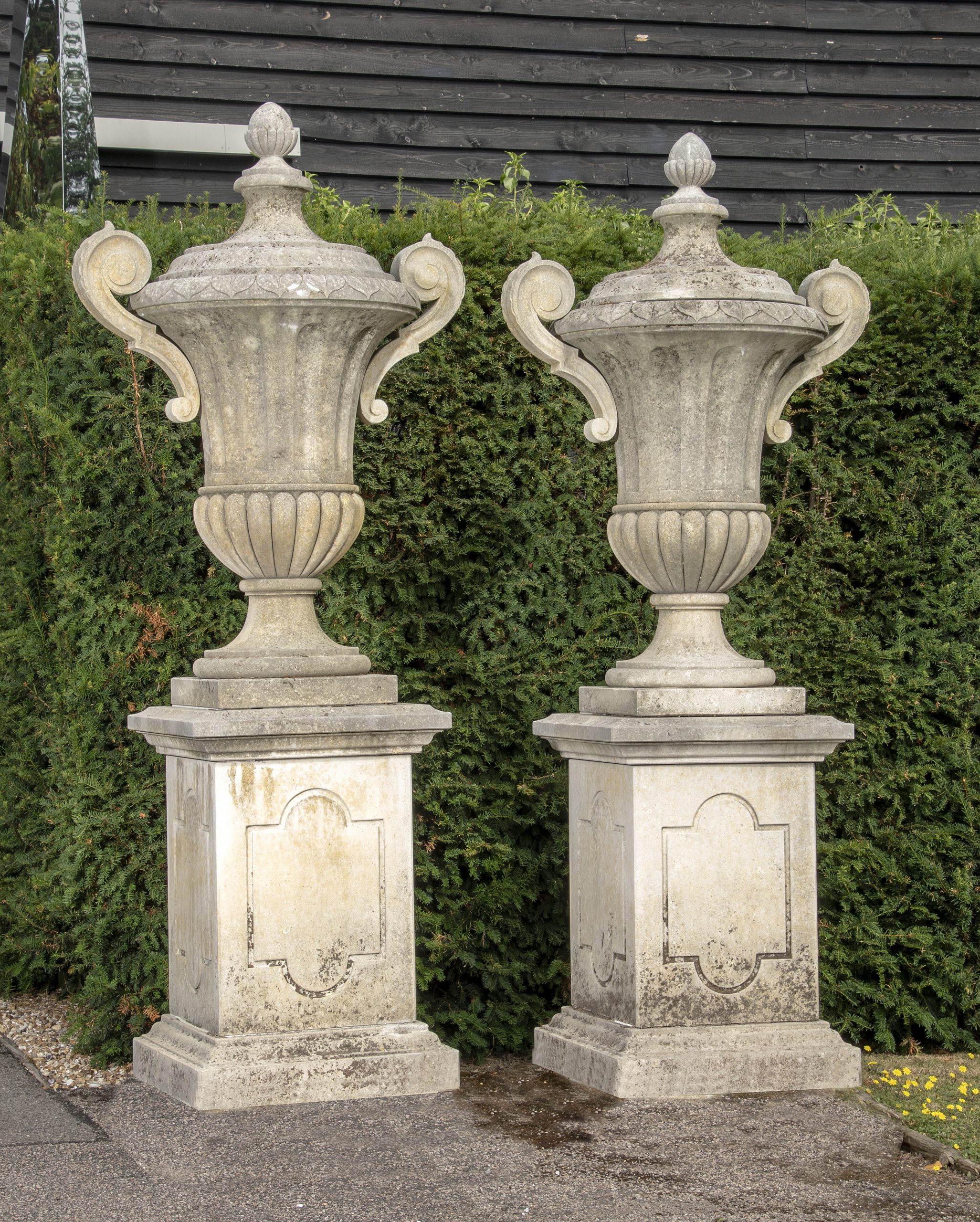 A pair of large carved limestone lidded urns with handles on pedestals